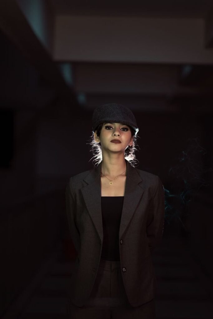 A stylish woman in a suit and hat poses dramatically in a dimly lit room.